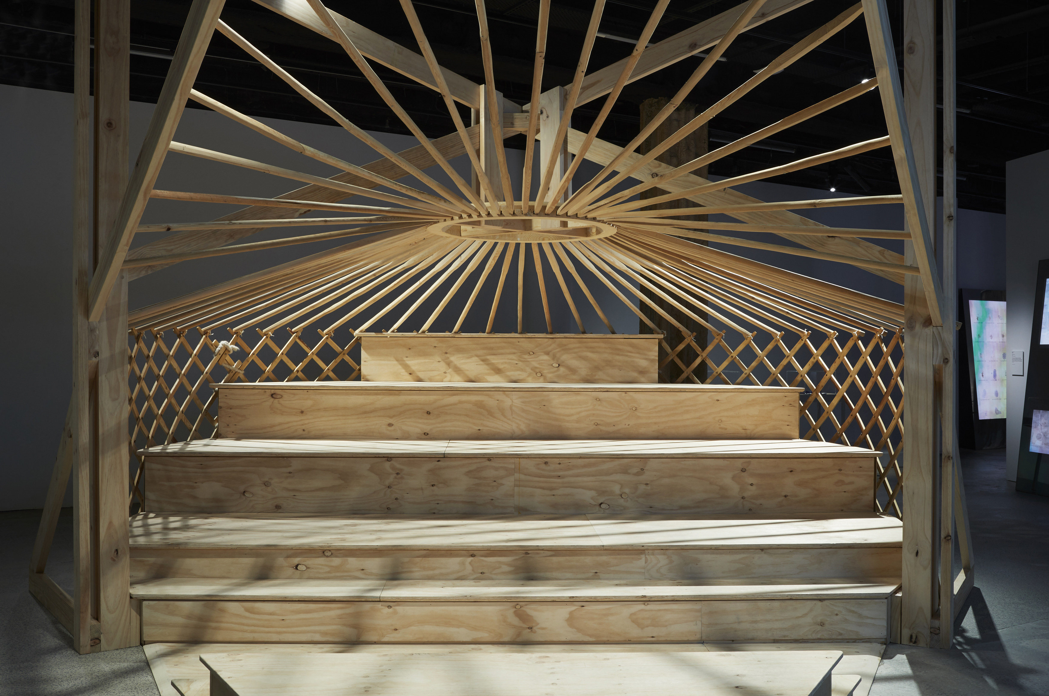 A five tiered wooden seating area with a latticed wooden framework behind and a central heating exhaust at the apex from which wooden beams connect to the latticed walls.